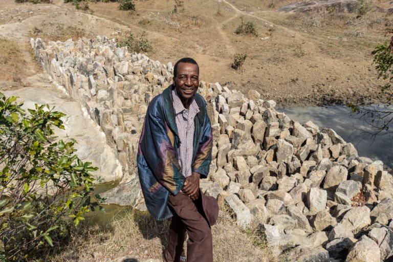 A man stands in front of a dam made of large rocks.