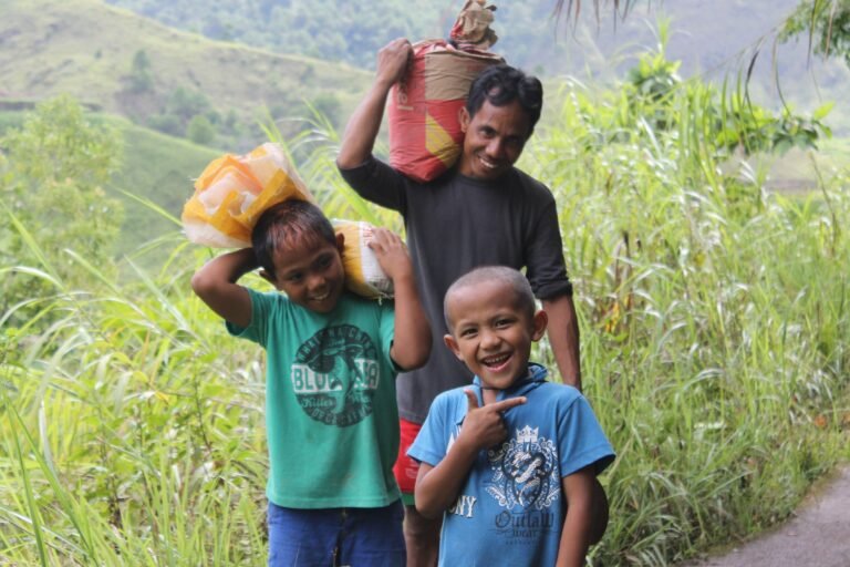 Two children and their father holding bags of rice on their shoulders and smiling.