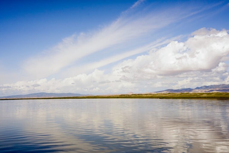 The water is reflecting the blue sky, mountains and clouds.