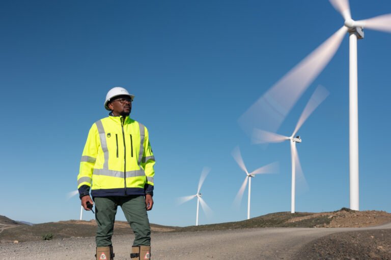 Man in fluorescent yellow vest and hard hat standing near wind turbines