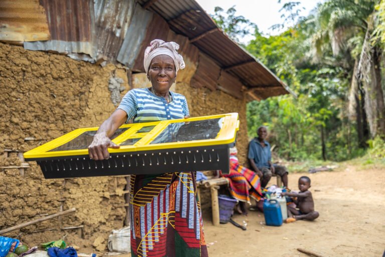 A female Liberian farmer holding a solar dryer.