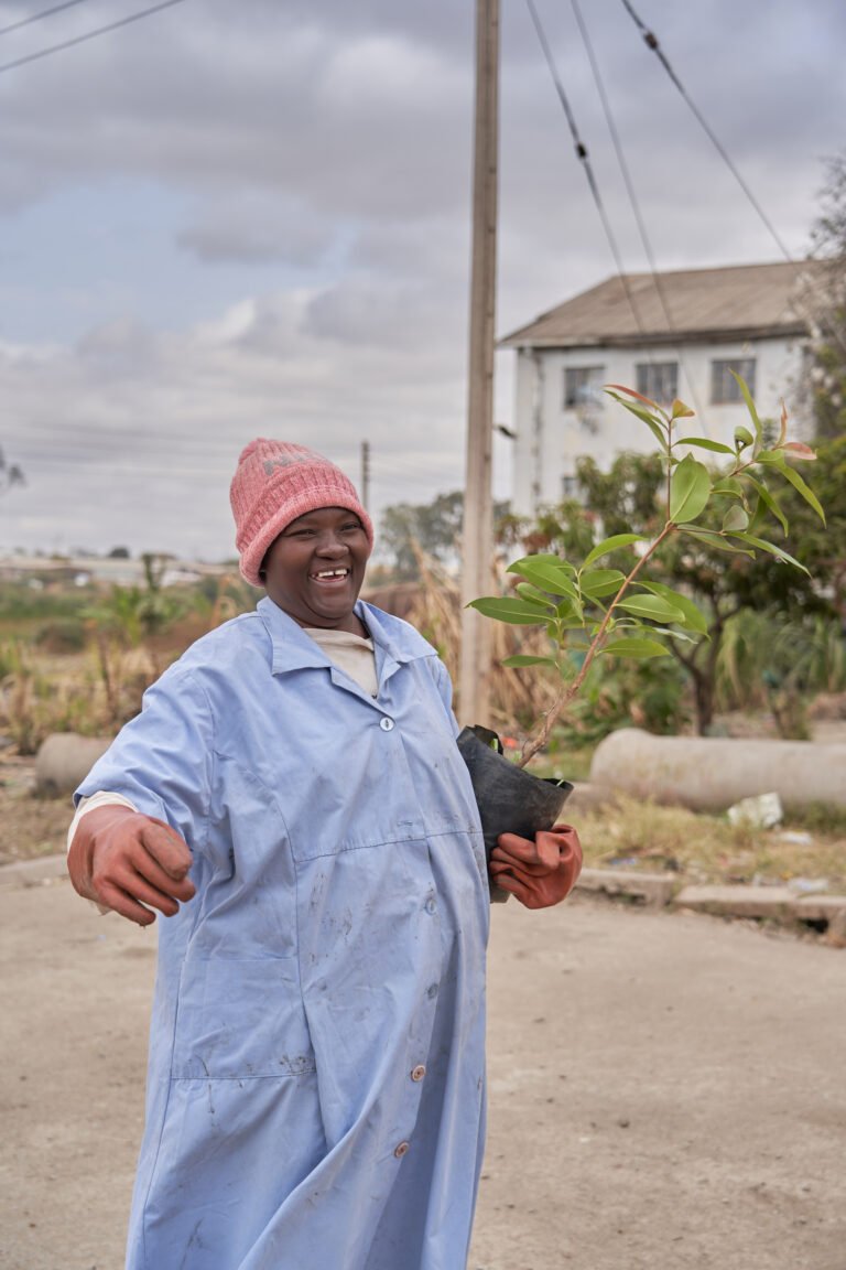 Female stands smiling holding tree in one hand as she prepares to do reforestation project in Zimbabwe