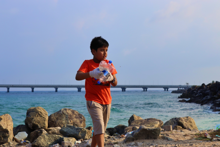 Boy standing on beach holding plastic bottles
