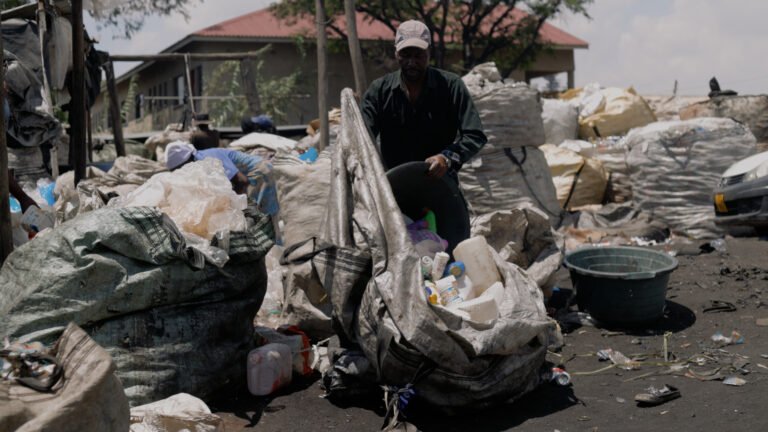 Man stands amongst rubbish in recycling centre