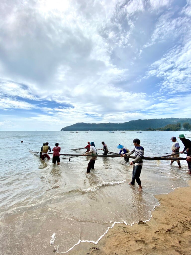 Several people pushing large trawling net into the ocean