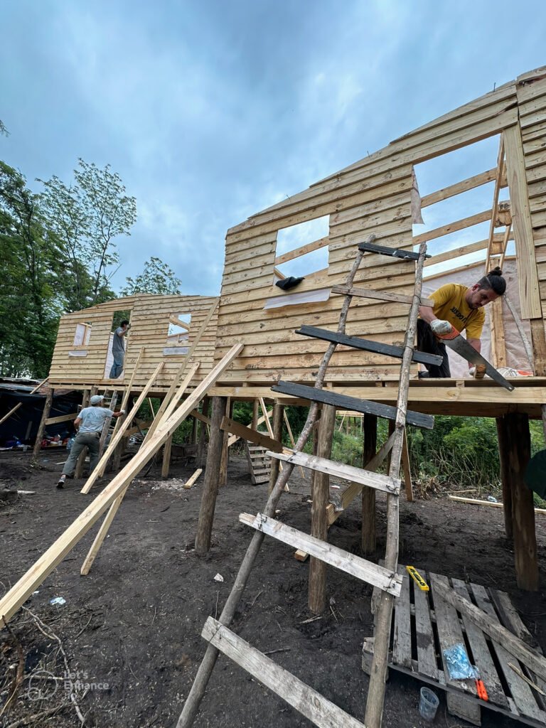 Two houses on stilts stand side by side as volunteers continue to build the homes.