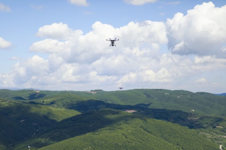 A drone flies in the cloudy sky over green fields.