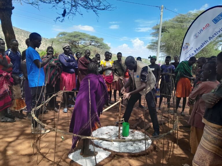 Man demonstrates the use of a water pump while a large group stands around him.