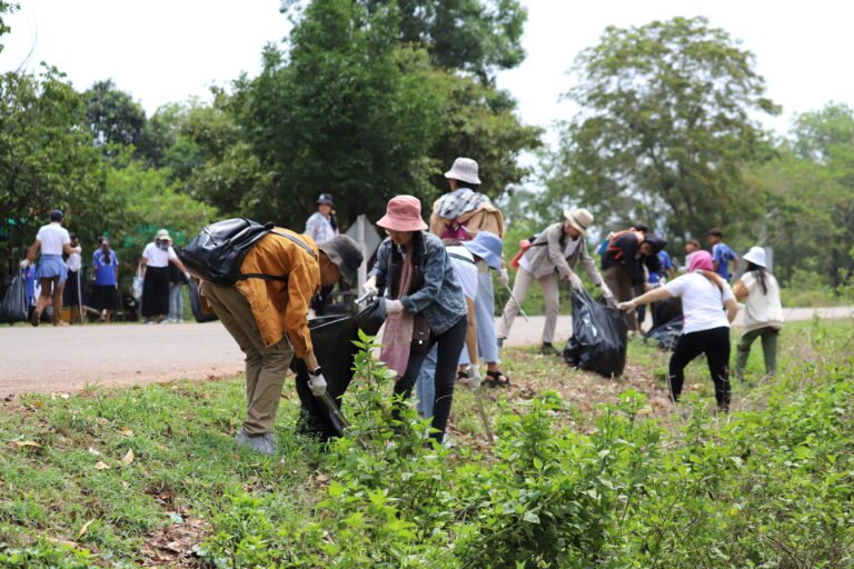A dozen young people picking up trash on the side of a road.