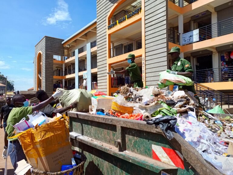 Two volunteers hand trash to two others in the rear of a dump truck in front of a market.