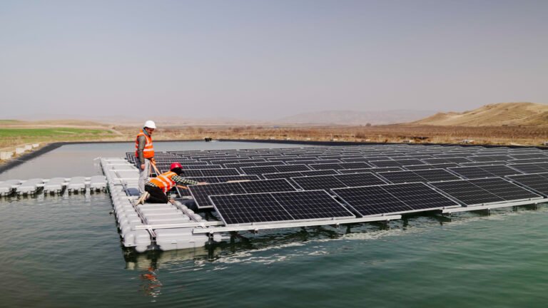 Two workers, one kneeling and one standing, work on the floating solar power station.