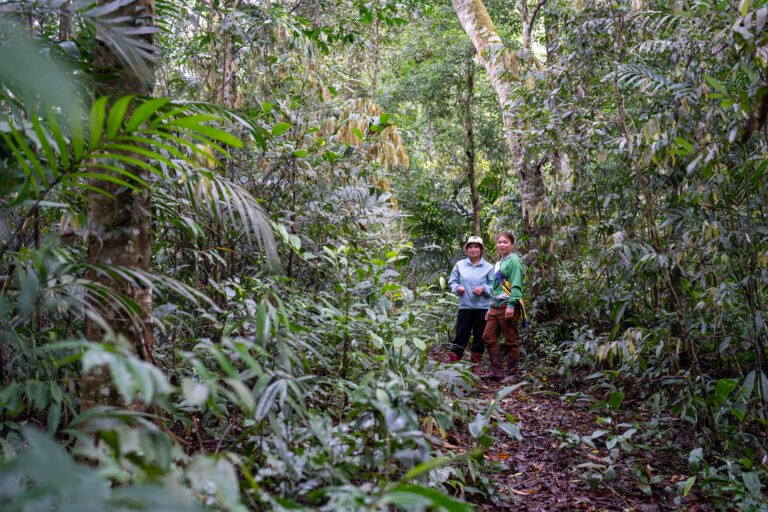 Two members of a community forest patrol stand together on a path in the forest.