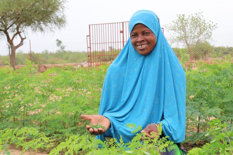 A woman stands among hip-length green crops.