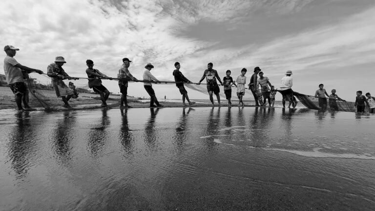 Black-and-white photograph of fisherfolk pulling a net on a beach.
