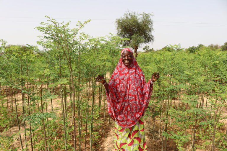 A woman smiles among rows of tall crops.
