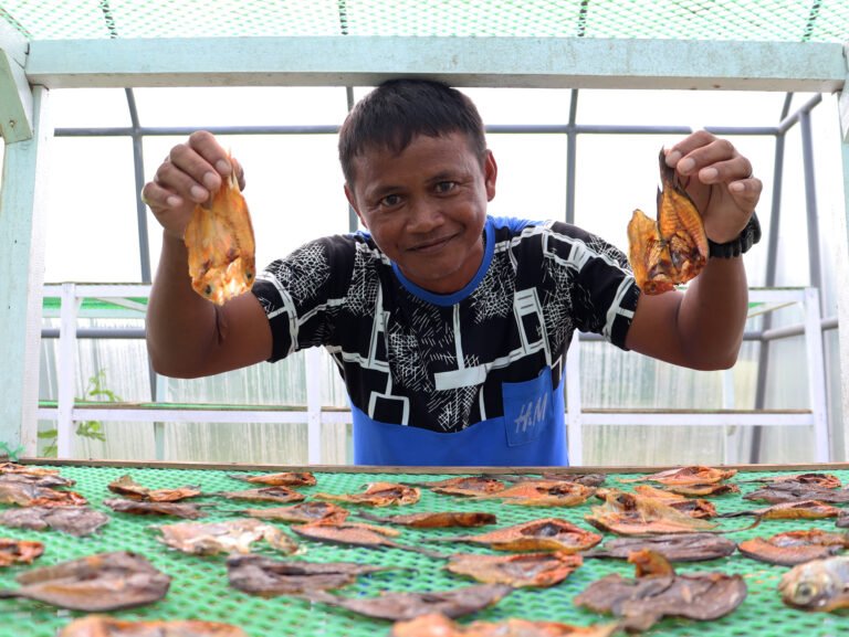 A fisherman holds up two dried fish as he sells his product at market.