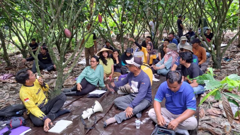 A group of people sit on the ground in a forest with papers and writing utensils.