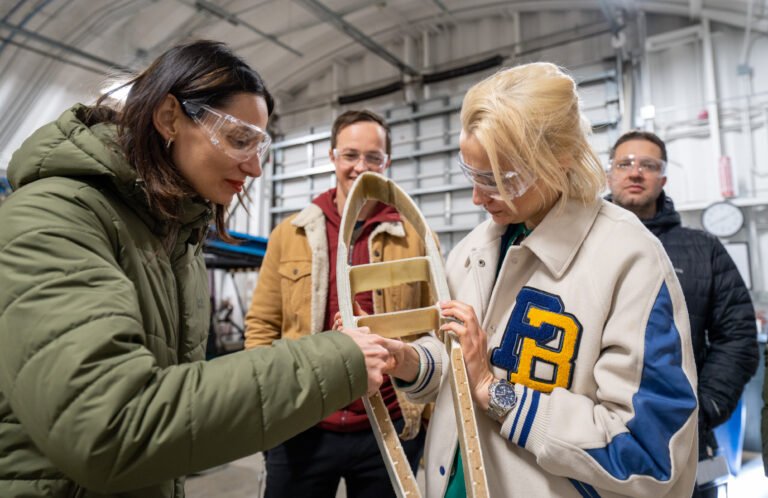 Two women in safety glasses examine something while two men look on.