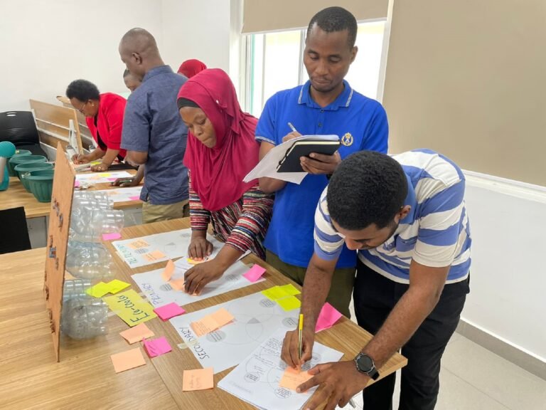 A group of people write on notebooks and sticky notes in a classroom setting.