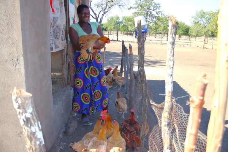 A woman smiles while holding a chicken with others around her feet.