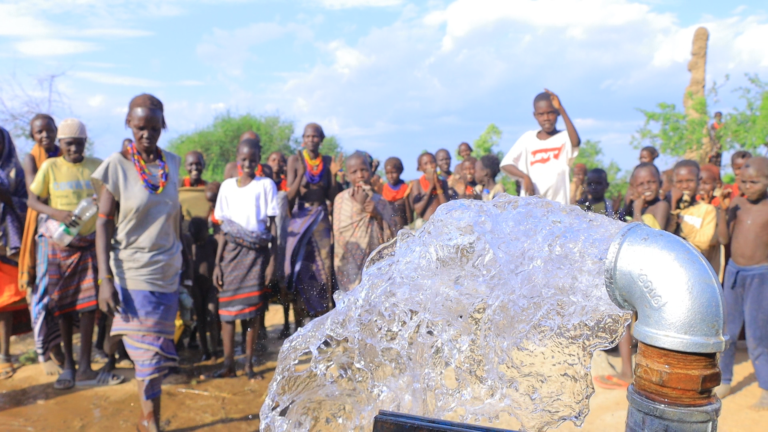 A group of people watch as water flows from a large pipe outside.
