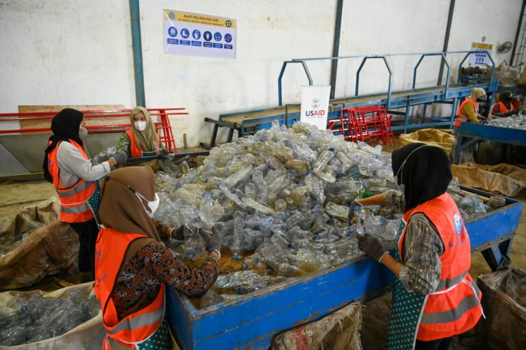 Four women sorting plastic bottles on a giant pallet.