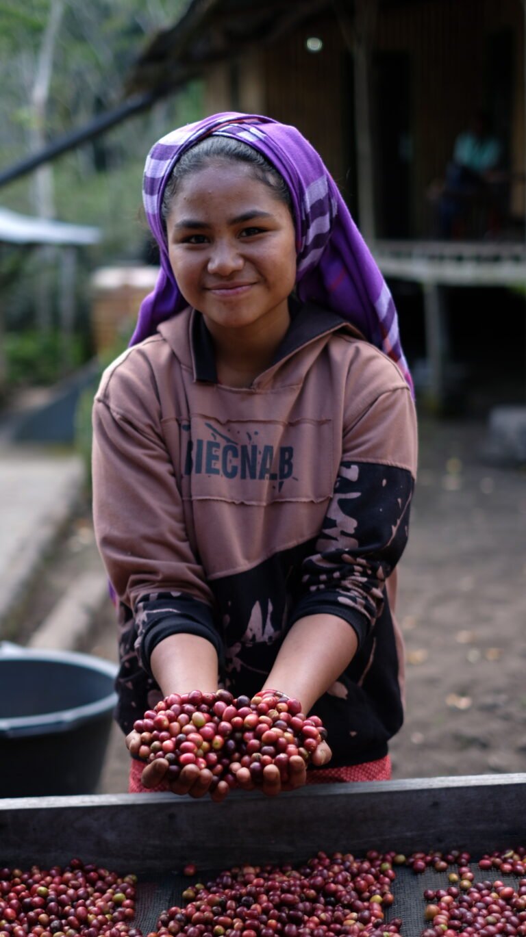 A young woman smiles at the camera while holding a handful of coffee cherries.