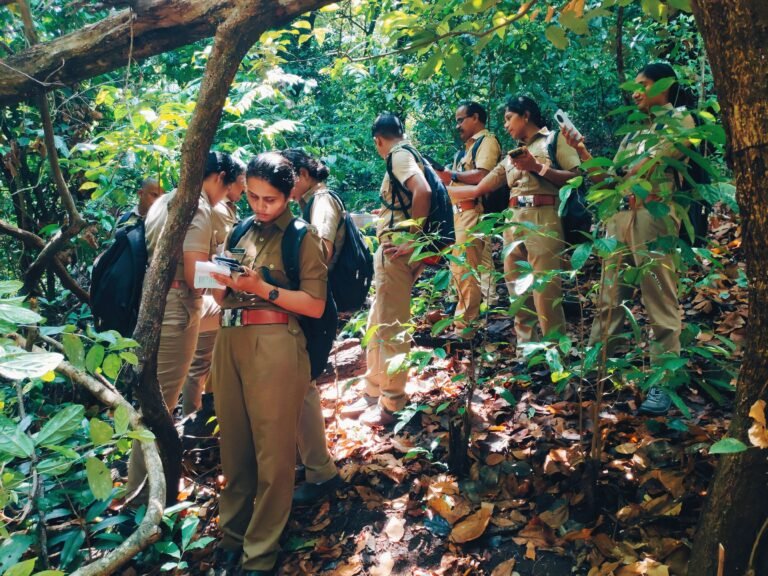 A group of people in uniforms stand in line in a forest as the leader looks down at a tool.