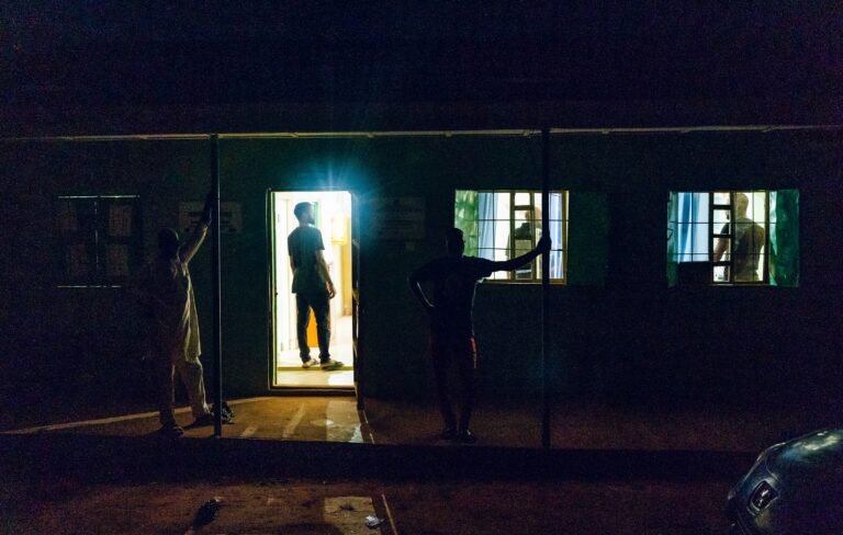 Abraham Bala Ezikiel stands in the doorway of a health facility at night time in Badariya, Birnin-Kebbi, Kebbi State, that just installed a solar powered source of light.