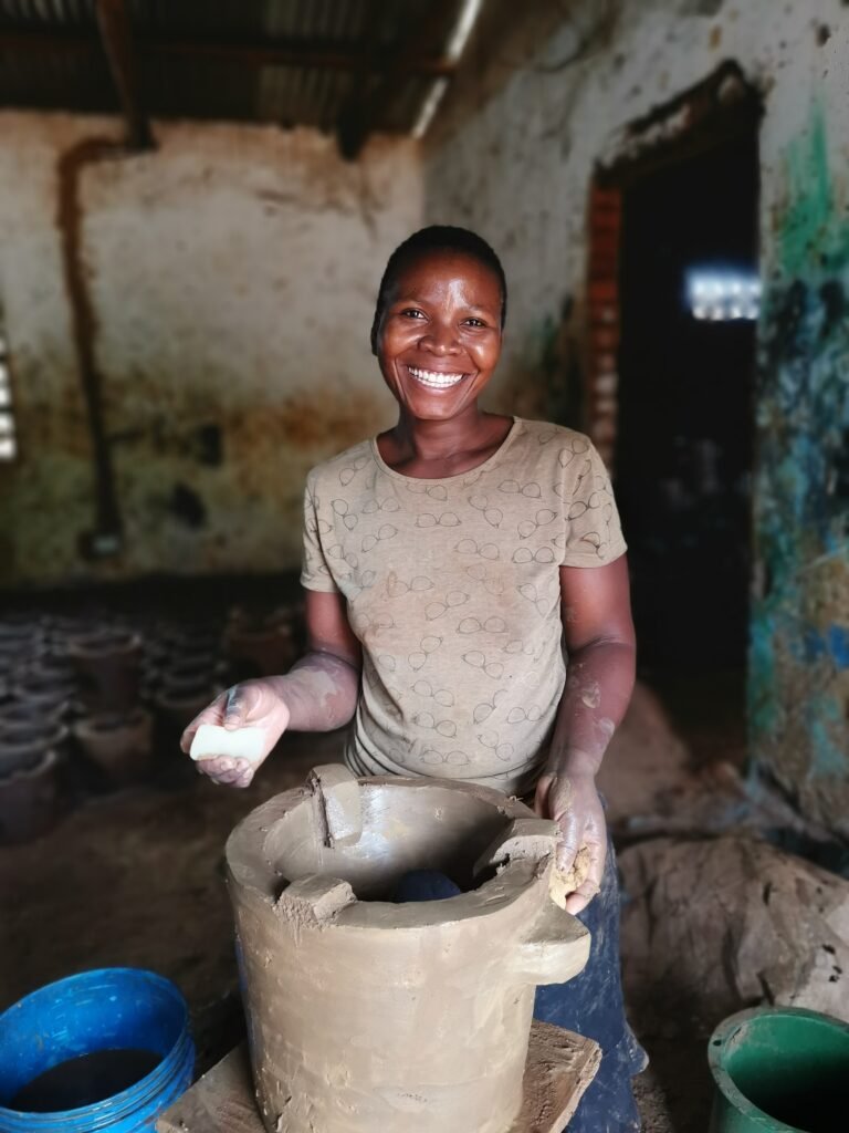 A woman smiles while cleaning a cookstove indoors.