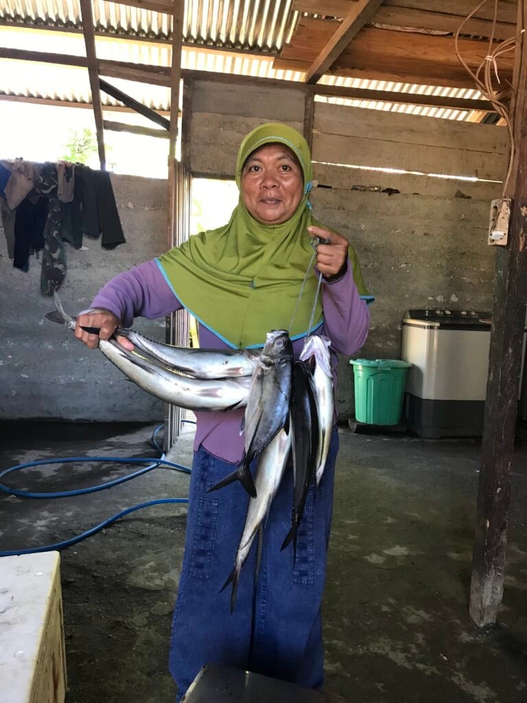 A woman shows off her fish catch in a warehouse.