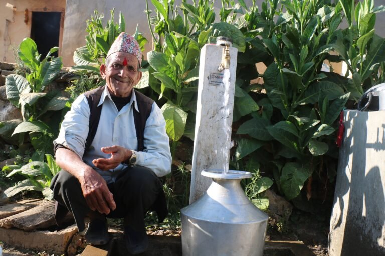 An older man crouched in front of a water tap.