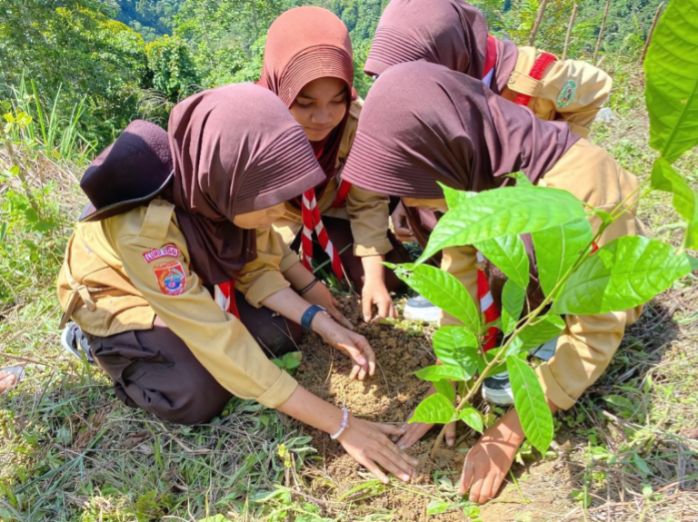 A small group of girl scouts wearing head scarfs plant a small tree sapling into the ground.