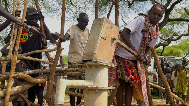 Several people pumping water from a borehole.