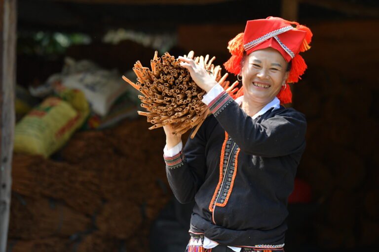 Woman holding a large bunch of cinnamon sticks over her shoulder smiles at the camera.