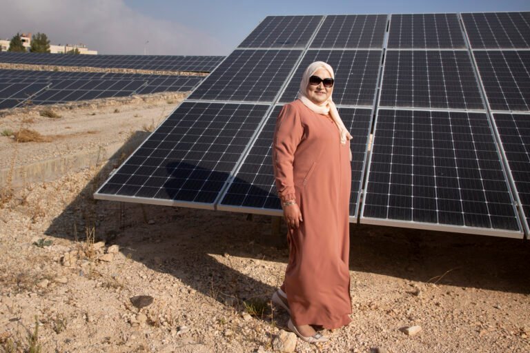 Woman in headscarf standing in front of large solar panel.