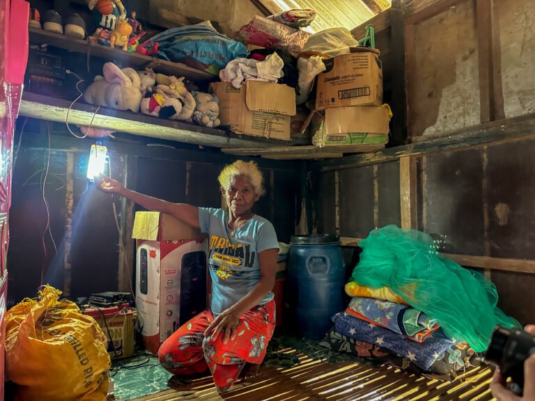 A woman kneels in her home in front of a lighted bulb.