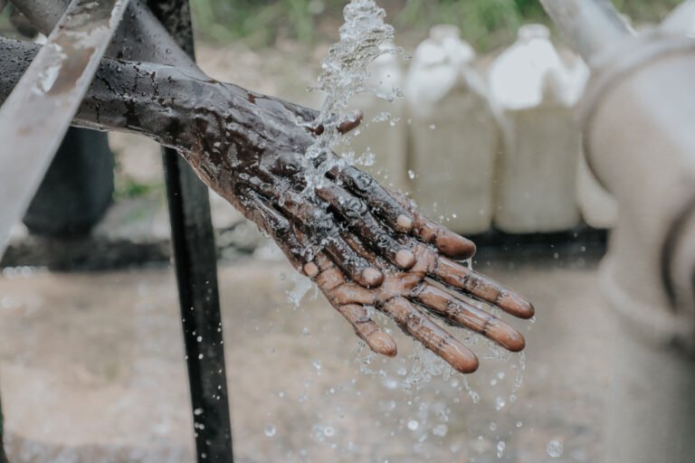 Hands being washed under an outdoor water source.