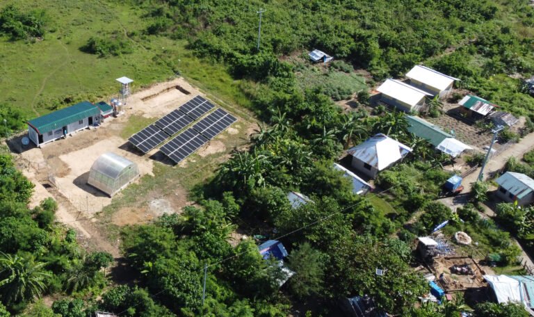 Aerial shot of solar panels and buildings in a clearing with trees.