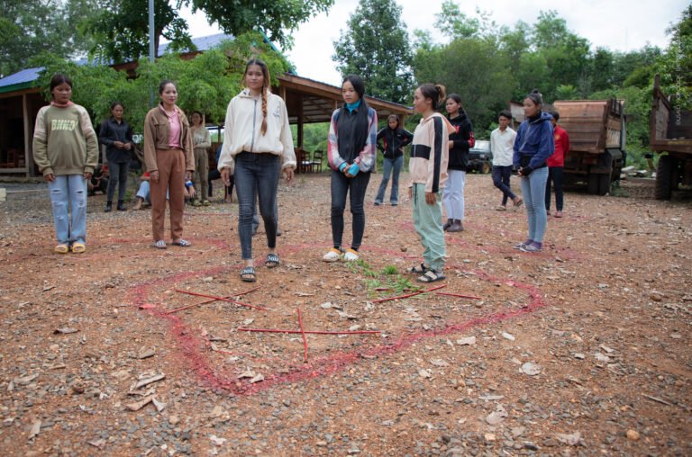Youth stand on the ground in an activity with red marks on the dirt.