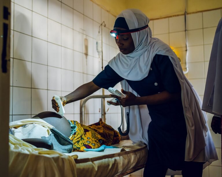 A health worker uses a headlamp as she examines a pregnant woman’s belly in a health facility.