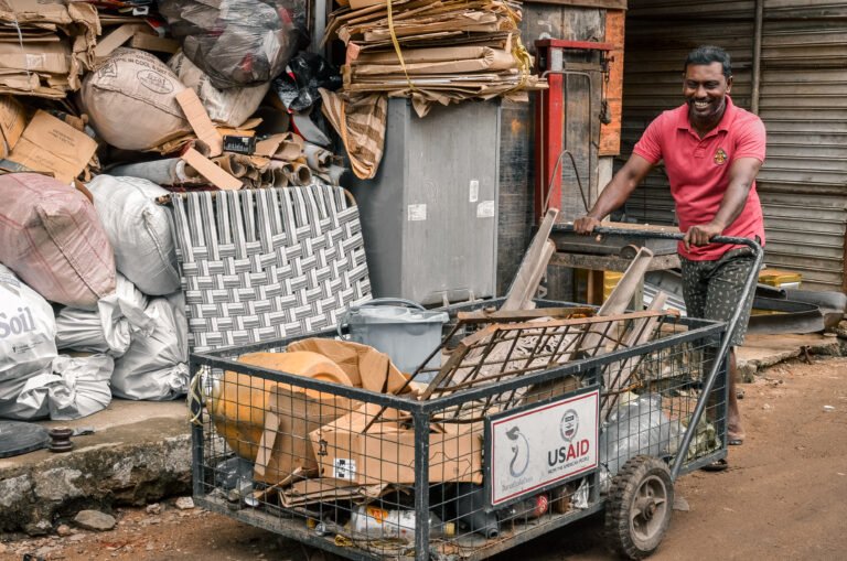 Man smiles while pushing an open cart with trash.