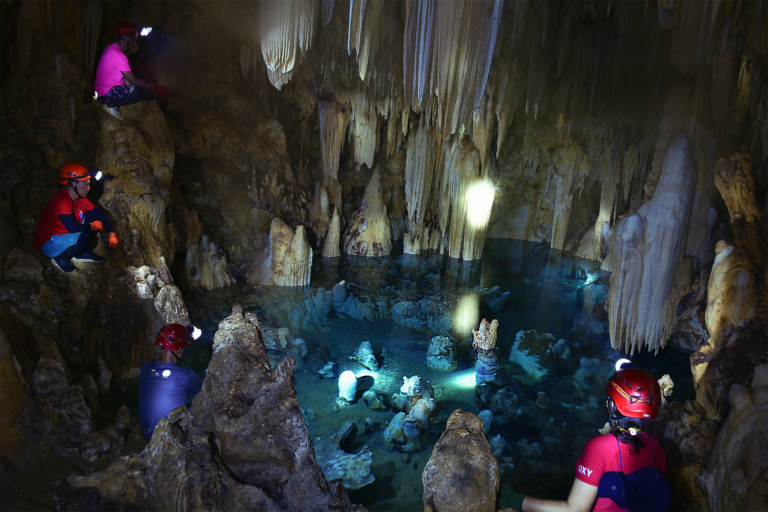 People wearing headlamps look down into a body of water in a cave.