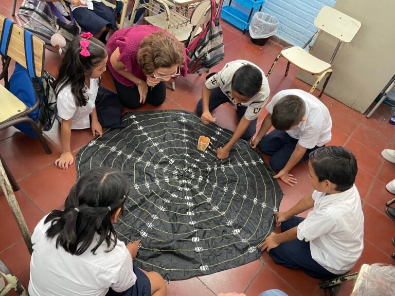Students and teacher gather around a recycled umbrella flattened on the floor of a classroom.