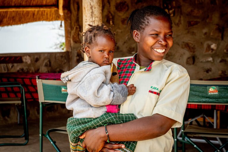 A woman smiles while holding her young daughter on her hip.