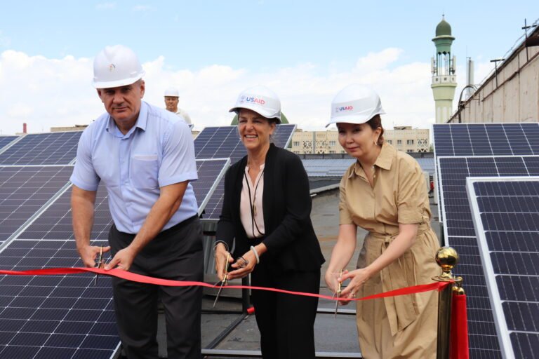 Three people cut a ribbon in front of solar panels on a rooftop.