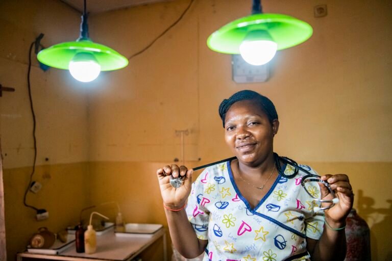 A nurse with a stethoscope around her neck smiles between two solar-powered lights.