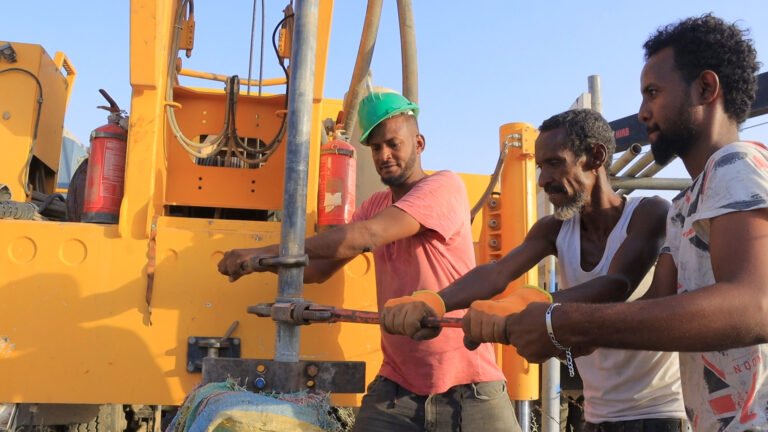 Three water technicians opening a borehole with machinery.