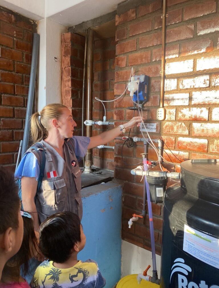 A Peace Corps volunteer points to a piece of water infrastructure while a group of students watch