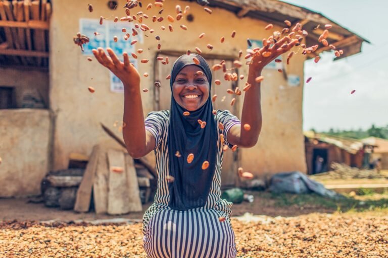 A woman smiles at the camera as she throws dried cocoa nibs into the air.